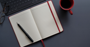notes na którym leży długopis, obok kubek, w lewym górnym rogu kawałek klawiatury
